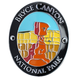 Könnte beinhalten: Eine schwarze und silberne Metallnadel mit einem bunten Bild des Bryce Canyon Nationalparks. Die Nadel zeigt eine rote und orangefarbene Felsformation mit blauem Himmel und gelben Canyonwänden.