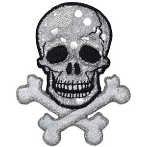 May include: A silver skull and crossbones patch with black outlines. The skull has a detailed design with a toothy grin.