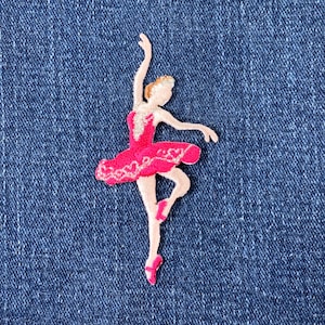 May include: A pink and white ballerina applique with a white background. The ballerina is wearing a pink tutu and white shoes.