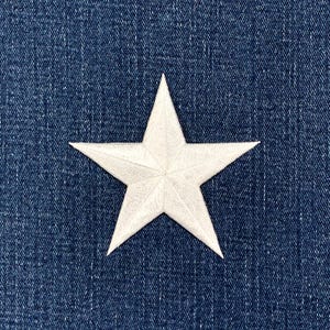 May include: A white star-shaped patch with five points, set against a blue denim backdrop. The star has a textured finish. The denim fabric has a classic, worn appearance.