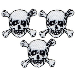 May include: Three white skull and crossbones patches. Each patch features a skull with a detailed design and crossed bones beneath. The patches are outlined in black and have a fabric texture.