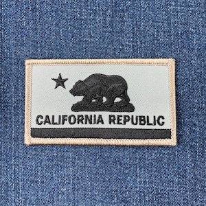 May include: A beige embroidered patch featuring a black bear silhouette and a star. The text "CALIFORNIA REPUBLIC" is written in black below the bear.
