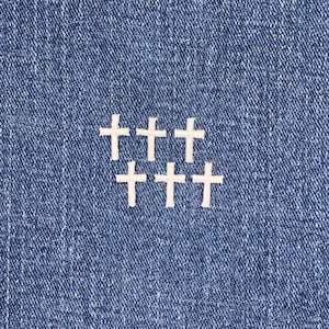 May include: Six white felt crosses arranged in a staggered pattern on a blue denim background.