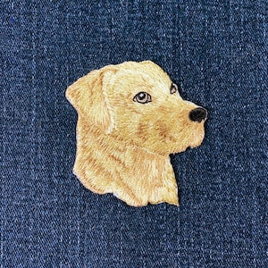 May include: Embroidered patch featuring a golden retriever dog head in profile. The patch is made with tan thread, showcasing the dog's fur, with black details for the eyes and nose. The patch is set against a dark blue denim background.
