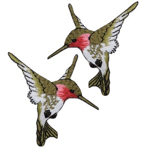 May include: Two embroidered hummingbird patches featuring olive green wings, white underbellies, and vibrant pink throat feathers. Each bird is depicted in a dynamic flying pose with wings extended, showcasing detailed stitching and long, thin beaks.