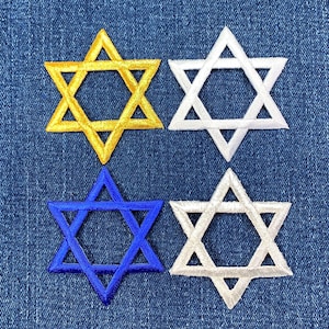 Peut inclure: Quatre patchs brodés en forme d'étoile de David de différentes couleurs : or, blanc, bleu et blanc. Les patchs sont sur un fond en jean bleu.