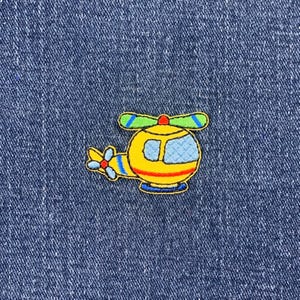 May include: A yellow helicopter with blue and green details is embroidered on a blue denim fabric.