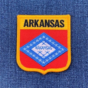 May include: A yellow, red, and blue embroidered patch with the word "ARKANSAS" in black lettering and a diamond-shaped design with the word "ARKANSAS" inside.