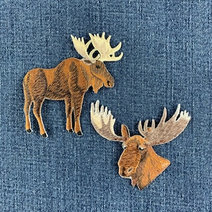 May include: Two embroidered patches featuring moose designs. One patch shows a full-body brown moose standing in profile with large cream-coloured antlers. The second patch depicts a brown moose head facing forward with wide, detailed antlers.
