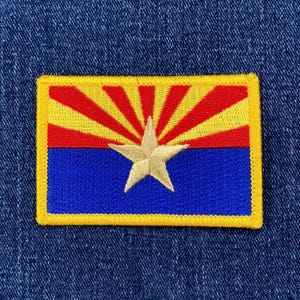 May include: Embroidered patch featuring the Arizona state flag. The patch has a rectangular shape with a yellow border. The design includes a blue lower section, a red and yellow sunburst, and a central gold star.