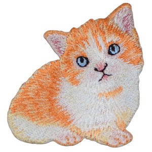 May include: A white and orange embroidered kitten patch with blue eyes. The kitten is sitting with its head tilted to the side.