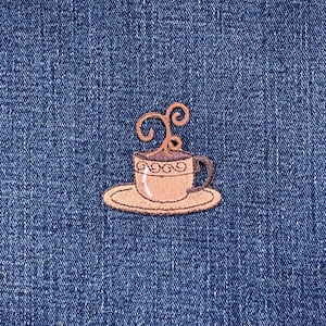 May include: Embroidered patch featuring a coffee cup with steam rising from the top. The cup and saucer are tan with brown accents. The patch is on a blue denim background.