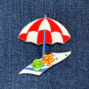 May include: Embroidered patch featuring a beach scene. A red and white striped umbrella is above a blue and white striped beach towel. A yellow starfish and green snail are on the towel. The patch is on a blue denim background.