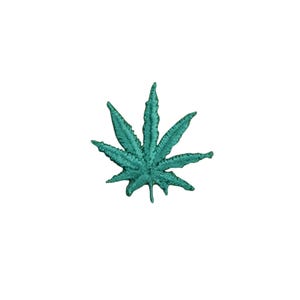 May include: A teal embroidered cannabis leaf patch. The patch features a detailed design of a seven-pointed leaf, with visible stitching and a textured appearance. The patch is set against a plain white background.