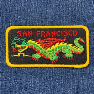 May include: A yellow and black embroidered patch with the text "SAN FRANCISCO" in red and a green and red dragon with yellow flames.