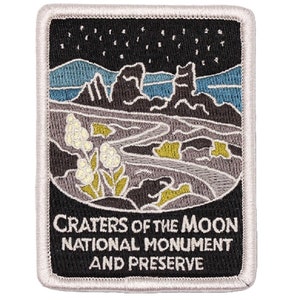 May include: A black and white embroidered patch with a gray, green, and blue landscape scene. The text "CRATERS OF THE MOON NATIONAL MONUMENT AND PRESERVE" is printed in white.
