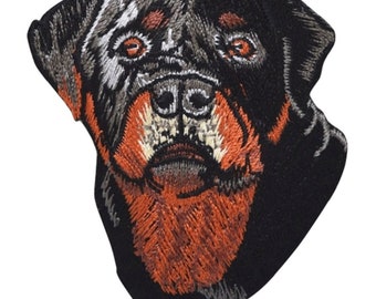 May include: Embroidered patch of a Rottweiler dog's face. The dog has black fur with tan markings around its eyes, nose, and mouth. The patch is made of black felt with embroidered details.