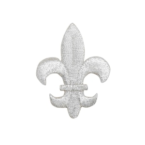 May include: A silver embroidered fleur-de-lis patch. The patch features a detailed design with a three-petal shape and curved accents. The embroidery has a textured appearance, and the patch is set against a white background.