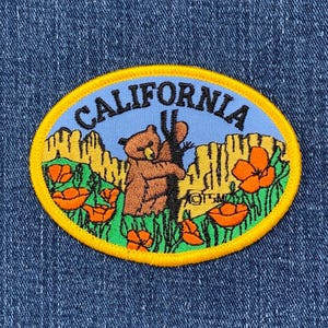 May include: A yellow and blue embroidered patch with the word "CALIFORNIA" in a black outline. The patch features a brown bear hugging a tree, surrounded by green foliage and orange poppies.