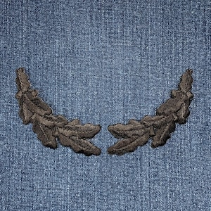 May include: A pair of black fabric leaves sewn together to form a wreath shape. The leaves are on a blue denim background.