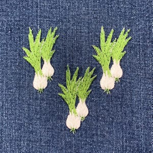 May include: Four embroidered green onion patches on a blue denim background. The onions are white and green with a detailed embroidered design.