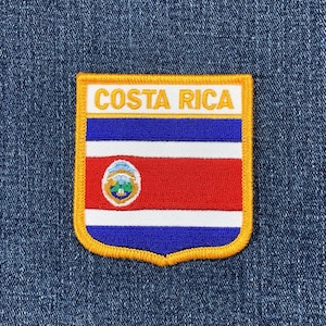 May include: Embroidered patch featuring the Costa Rican flag design. The patch has a white border with the words "COSTA RICA" in gold lettering. The flag design includes blue and red stripes, and a central emblem.