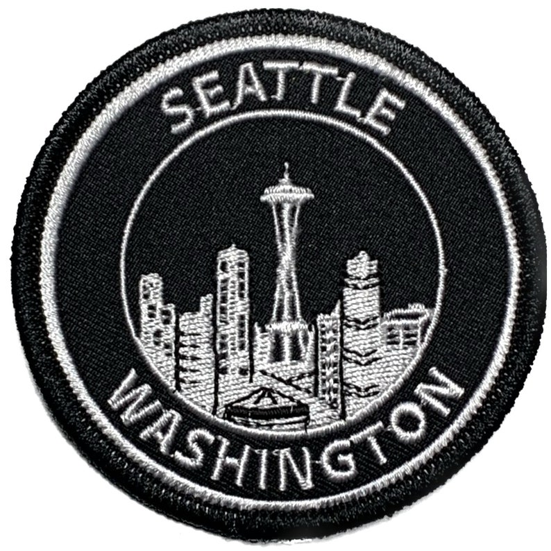 May include: Black and white embroidered patch with a circular design. The center of the patch features a white silhouette of the Seattle skyline, including the Space Needle. The text "SEATTLE WASHINGTON" is written in a white circular border around the skyline.