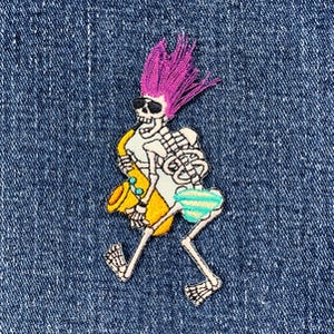 May include: Embroidered patch featuring a skeleton playing a yellow saxophone. The skeleton has pink hair, sunglasses, and blue and white striped shorts. The patch is on a blue denim background.
