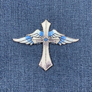 May include: A silver cross with blue and white wings, embroidered on a denim background.