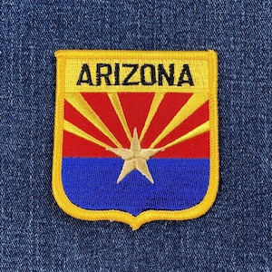 May include: Embroidered Arizona state patch with a shield shape. The patch features a yellow border, the word "ARIZONA" in black, a red and yellow sunburst design, a blue base, and a gold star in the center.
