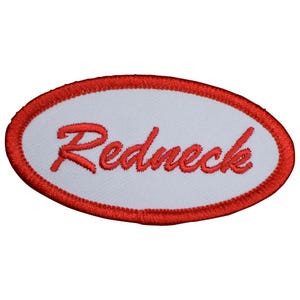 May include: An oval-shaped embroidered patch featuring a white center background with a thick red stitched border. The word Redneck is embroidered in red cursive script across the center of the patch, creating a bold and clear visual contrast.