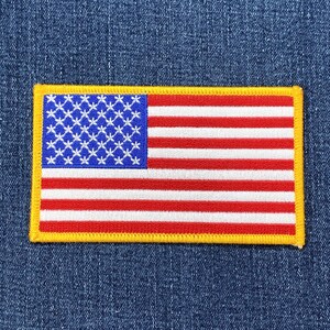 May include: A rectangular patch depicting the American flag. The flag shows a blue canton with white stars, and red and white stripes. The patch is edged with a yellow border.