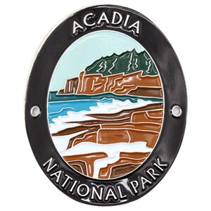 May include: A black and silver metal round pin with a white, blue, and green image of a rocky coastline and ocean waves. The text "Acadia National Park" is written around the image.