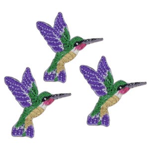 May include: Three embroidered hummingbird patches featuring vibrant purple wings, green bodies, and tan underbellies. Each bird is depicted in a mid-flight position with a long, thin beak, a small black eye, and a touch of pink coloring near the throat area.