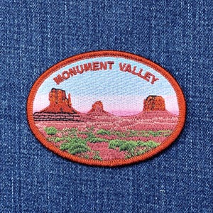 May include: Oval patch featuring a landscape of Monument Valley. The patch has a red border and includes the text "MONUMENT VALLEY" in red. The landscape depicts red rock formations, green shrubbery, and a pink and blue sky.