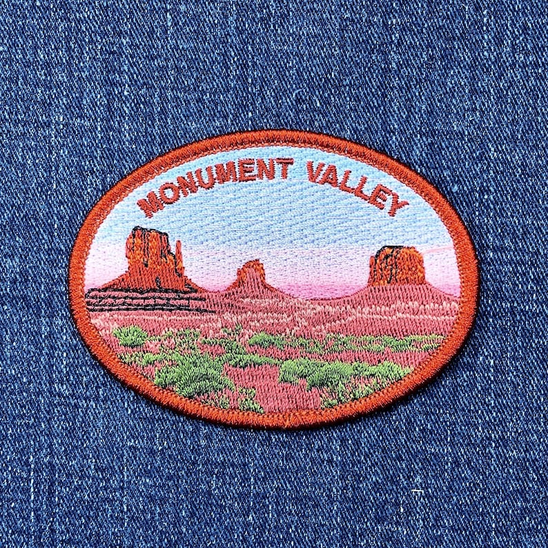 May include: Oval patch featuring a landscape of Monument Valley. The patch has a red border and includes the text "MONUMENT VALLEY" in red. The landscape depicts red rock formations, green shrubbery, and a pink and blue sky.