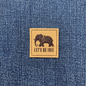 May include: A square, tan patch with a dark brown elephant silhouette and the text "LET'S BE IRIE" in a serif font. The patch is set against a blue denim background.