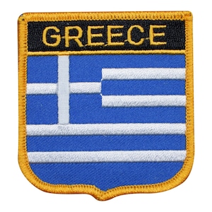 Könnte beinhalten: Ein gestickter Aufnäher mit der griechischen Flagge in Blau und Weiß, mit dem Wort "GREECE" in gelben Buchstaben auf schwarzem Hintergrund. Der Aufnäher ist mit einem goldenen Rand versehen.