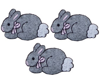 May include: Three gray felt bunny rabbit appliques with pink bows. Each bunny is lying down with its head turned to the side.