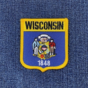 May include: A blue, yellow, and white embroidered patch featuring the word "WISCONSIN" at the top. The patch has a blue background with a state seal design and the number "1848" at the bottom. The patch is rectangular with rounded corners.