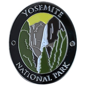 May include: Oval-shaped pin featuring the Yosemite National Park logo. The design includes a waterfall, mountains, and trees, with the words "YOSEMITE NATIONAL PARK" in white lettering on a black border. The background is green, gray, and yellow.