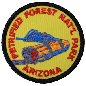 以下が含まれることがあります： 「Petrified Forest Natl Park Arizona」という文字が書かれた黄色と赤の刺繍パッチ。パッチには、化石化した丸太のスタイリッシュな画像が描かれています。