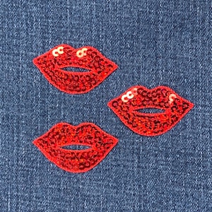 Könnte beinhalten: Drei rote Pailletten-Lippen-Patches auf einem blauen Jeans-Hintergrund.