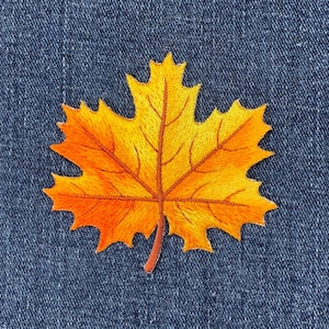 May include: A close-up of an orange and yellow embroidered maple leaf patch on a blue denim background.