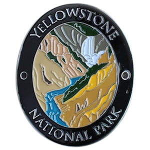 May include: A black and silver metal Yellowstone National Park collector's pin with a colorful enamel design of a landscape scene. The pin features the words "Yellowstone National Park" around the edge.