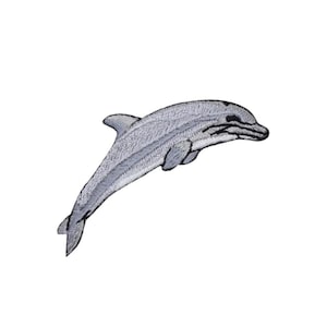 Könnte beinhalten: Gestickter Aufnäher mit einem grauen Delfin, der aufspringt. Der Delfin hat detaillierte Stickereien mit einer dunkleren grauen Umrandung und schwarzen Akzenten an Auge und Maul. Der Aufnäher befindet sich auf weißem Hintergrund.