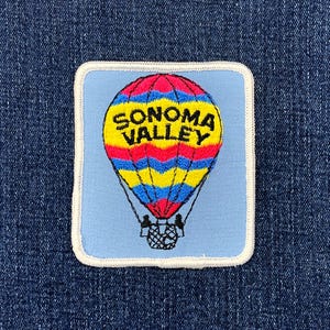 May include: Embroidered patch featuring a colorful hot air balloon with the text "SONOMA VALLEY" in yellow. The balloon has red, blue, and yellow stripes. The patch is on a light blue background with a white border.