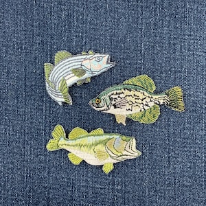 May include: Three embroidered fish patches featuring detailed stitching. The top left patch is a light blue and white striped fish. The middle right patch is a green and black mottled fish. The bottom patch is a light green and yellow fish.