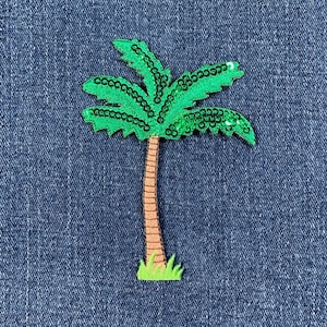 May include: A green sequined palm tree patch with a brown trunk and green grass at the base, set against a blue denim background. The palm tree design is a tropical theme.