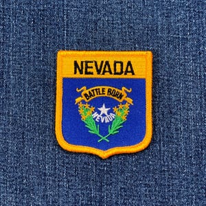 May include: A rectangular patch featuring the Nevada state seal. The patch has a gold border and a blue center with the words "NEVADA" at the top. The seal includes text "BATTLE BORN" and a star.